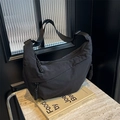 Minimalist black crescent crossbody bag with braided rope zipper pulls on marble - Black