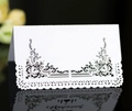 Elegant white laser-cut wedding place card with black vintage scrolls on black background - White