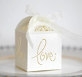 Macro shot of white laser-cut wedding candy box with gold LOVE text and ribbon bow - Ivory