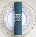Detailed close-up of hollow silver napkin ring with dark green fabric on white dinnerware - Reflective Silver