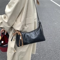 Minimalist black glossy shoulder bag with brown woven charm worn with beige coat - Black