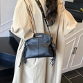 Black leather tote bag with long tassels and eyelet strap worn cross-body style - Black