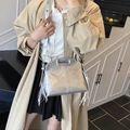 Silver metallic crossbody bag with long tassels and cutout handle held by model - Silver
