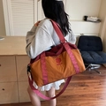 Large orange travel bag with maroon straps shown being worn by a female model - Brown