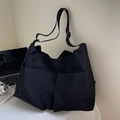 Minimalist black nylon crossbody tote bag with dual front pockets in a workspace setting - Black