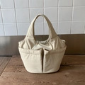 Dettaglio borsa a secchiello in nylon crema con grandi tasche anteriori su legno scuro - Bianco Sporco