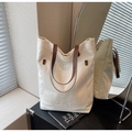 Détail du sac cabas en toile montrant le tissu crème, l'anse en cuir marron et le rivet - Blanc Cassé