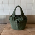 Dettaglio della borsa a secchiello verde scuro con tasche frontali su legno - Verde