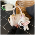 Détail du sac oreiller crème avec gaufrage d'ours et breloque lapin en peluche à la main - Rose avec pendentif