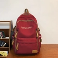 Dunkelroter Canvas-Rucksack mit Frontlogo und Leder-Zippern auf Holzoberfläche - Rot