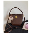 Detail of a dark brown suede bucket bag featuring a gold twist lock and a cute plush bear charm - Coffee