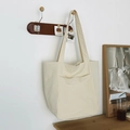 Minimalist off-white canvas tote bag with front pockets hanging in home setting - Light Camel