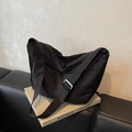 Minimalist black oversized crossbody bag with wide adjustable strap on a leather sofa - Black