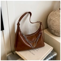 Detail of brown leather tote bag with stylish silver chain strap on a white book - Brown