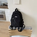 Minimalist black nylon backpack with brand label on a stylish wooden stool - Black