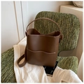 Detailed view of a brown leather bucket bag with white contrast stitching on a green chair - Brown