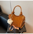 Dettaglio della pelle goffrata di una borsa a secchiello marrone con ciondolo peluche - Marrone