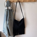 Retro black suede fringe shoulder bag hanging on a hook with casual lifestyle props - Black