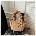 Detalle de bolso de ante beige con diseño plisado y lazo decorativo sobre maleta - Caqui