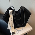Matte black suede tote bag with V-shaped opening and lettered strap detail on white book - Black