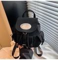 Detail of black matte fabric backpack featuring an oval metal logo plate and side buckles - Black