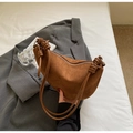 Détail du sac croissant en daim marron avec nœud en cuir tressé sur lit blanc - Marron