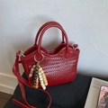Detail einer dunkelroten geflochtenen Handtasche mit Perlenquasten und Silberring - Rot