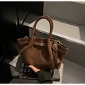 Detalle de un bolso cubo de ante marrón oscuro con correas decorativas y hebilla dorada - café