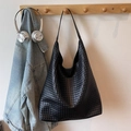 Large black woven hobo shoulder bag hanging on wooden rack with casual accessories - Black