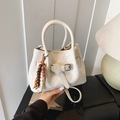 Cream white woven bucket bag with beaded charm and top handle in a cozy lifestyle setting - Beige With Charm