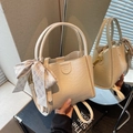 Detail view of a cream bucket bag featuring a silk scarf bow and embossed logo text - Off-white