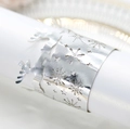 Close-up of laser-cut silver napkin rings featuring reindeer and snowflake patterns - Reflective Silver