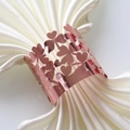 Detailed close-up of rose gold cutout clover napkin ring on a white satin cloth - Mirror Rose Gold