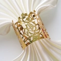 Close-up of golden rose hollow napkin ring on white satin fabric for wedding table decor - Sparkling Gold