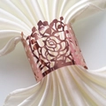 Close-up of laser-cut rose gold napkin ring with hollow floral pattern on white silk - Mirror Rose Gold