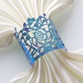Macro detail of iridescent laser-cut rose napkin ring on elegant white satin napkin - Rainbow Blue