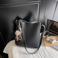Minimalist black lychee leather bucket bag featuring a cute brown plush monster charm - Black