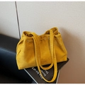 Detail of mustard yellow suede tote bag featuring drawstring accents on a fashion magazine - Yellow