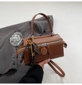 Detail of brown cylinder Boston bag featuring a gold key charm and dual zipper closure - With Ornament / Brown