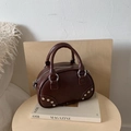 Bolso tipo almohada en ecocuero marrón oscuro con remaches sobre mesa de madera - Marrón