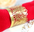 Dettaglio portatovagliolo dorato traforato con motivo floreale su tessuto rosso - Oro Riflettente