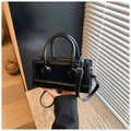 Detailed shot of black leather handbag featuring silver buckle and adjustable shoulder strap - Black