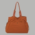 Detail of water-resistant orange nylon tote bag showing front snap pocket and side drawstrings - Orange