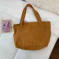 Detail of caramel canvas tote bag with long shoulder straps on a cozy white bed setup - Orange