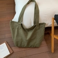 Detalle de un bolso tote de lona verde oscuro grande colocado sobre cama blanca y madera - Verde