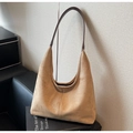 Close-up of brown suede hobo bag with leather strap leaning against a black leather chair - Khaki