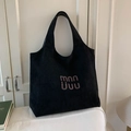 Black suede tote bag featuring a purple artistic logo on a white sofa background - Black