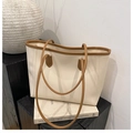Détail du sac cabas crème avec bordure en cuir marron posé sur un socle décoratif - Blanc