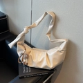 Beige halve maan schoudertas met geknoopte riem en monsterbedeltje op een lederen stoel - Off-wit