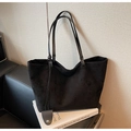 Close-up of black suede tote bag with leather strap and decorative charm on a sofa - Black
